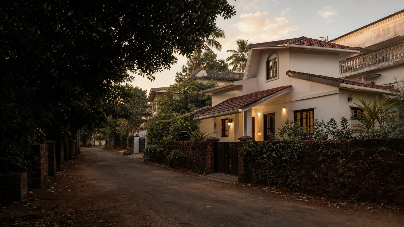 A lane at dusk, a house lit behind a laterite wall