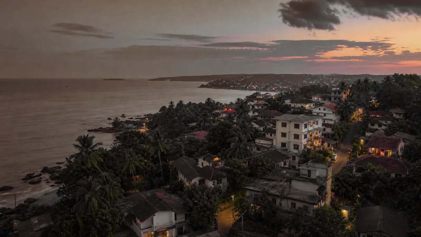 A coastal town at dusk, houses lit among the palms